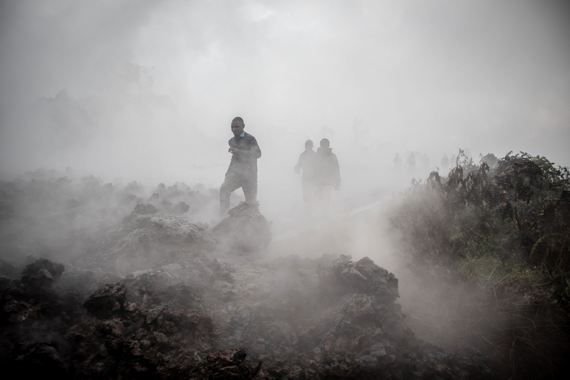 North Kivu, 23 May 2021. On the morning after the eruption Congo in Conversation photographer Guerchom Ndebo continued to file photographs for Agence France-Press, including this image of people crossing lava still smouldering and releasing noxious gases as it cools. 