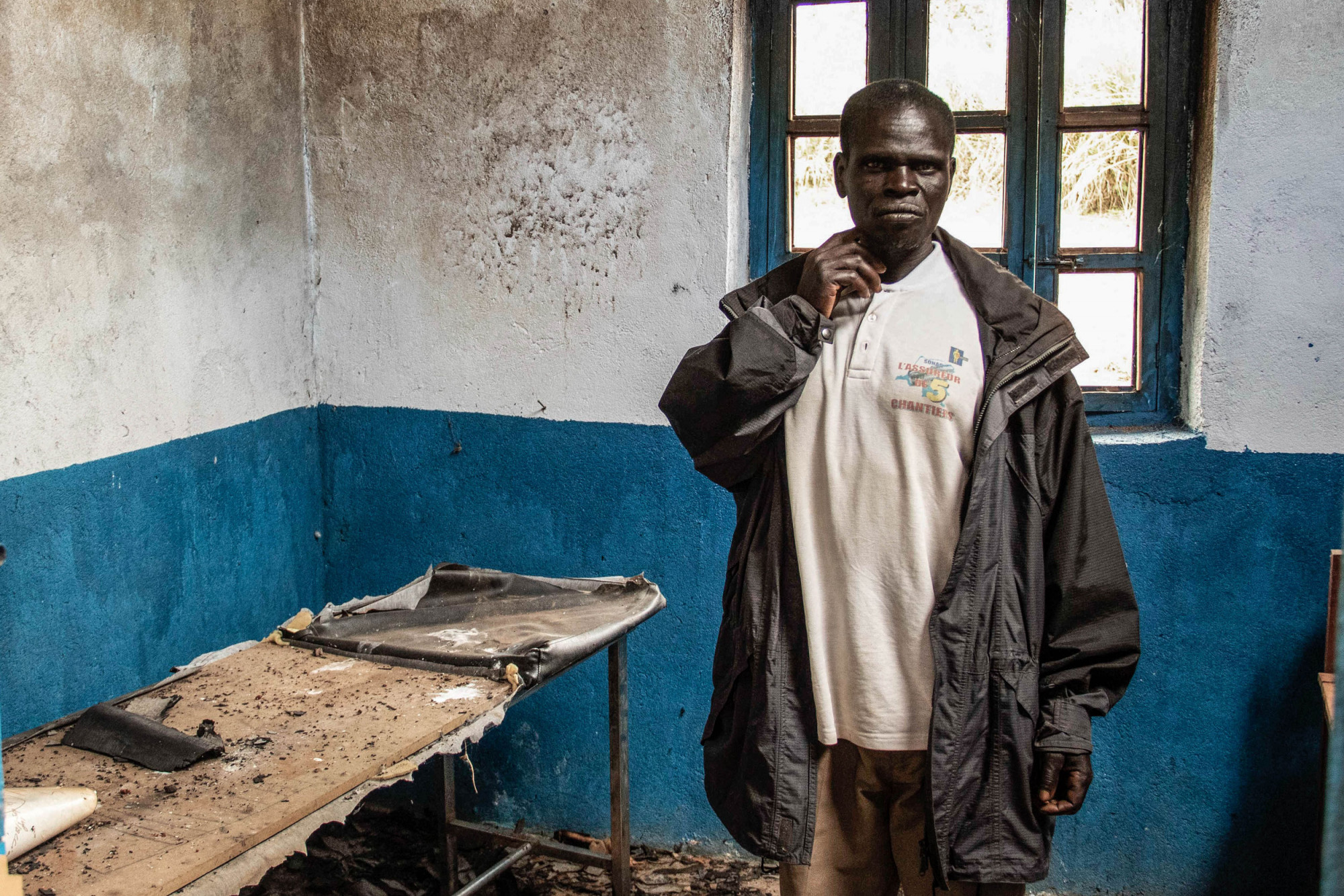 Tche, DRC, February 2020. A village chief stands in the destroyed health clinic in the village of Tche in Ituri province in February. A series of massacres in villages in Djugu territory, including Tche, killed 161 people in early June 2019 and killings in the area have continued in 2020. Hospitals and health clinics have been destroyed and burned during the ongoing conflict between the Hema and Lendu ethnic groups in the area. © Dieudonne Dirole for Fondation Carmignac